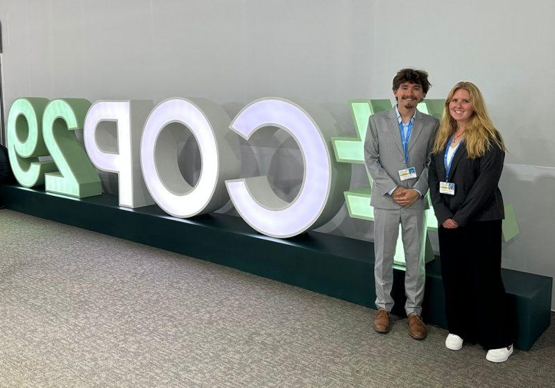 Woman and man in professional dress stand in front of large letters.